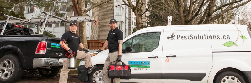 Solutions Pest Control service technicians with their trucks outside large condo building